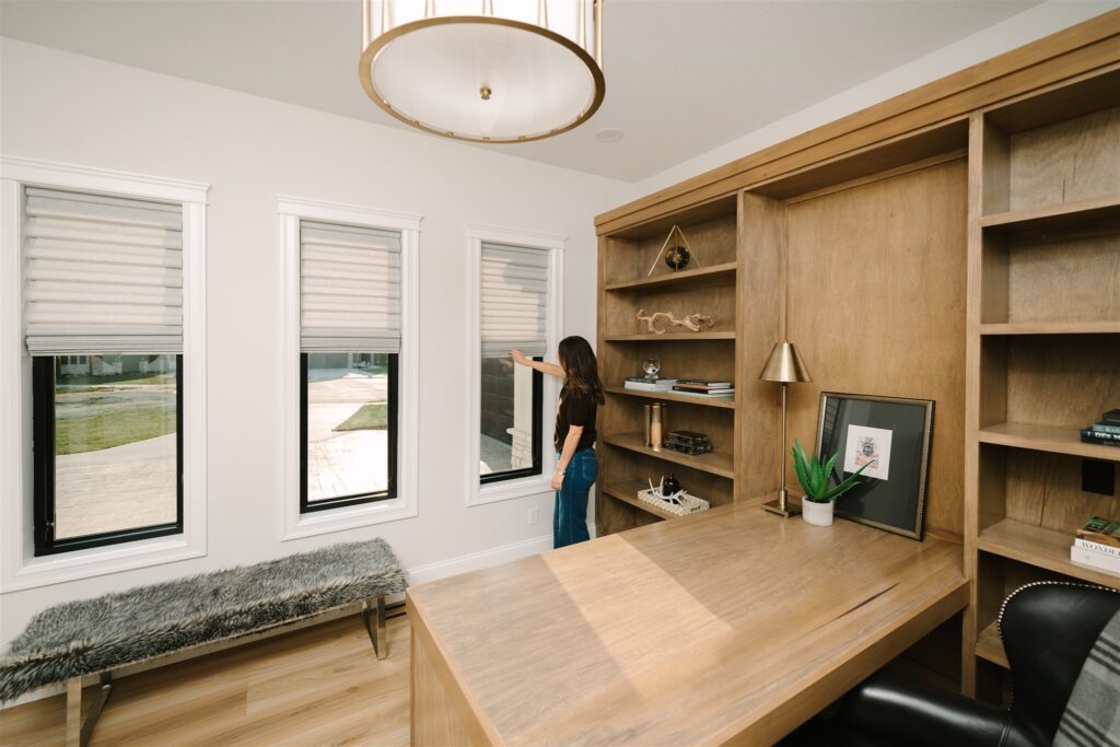 Home office desk beside three gray Roman shades installed on narrow windows.