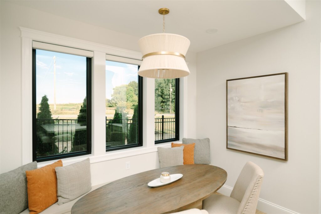 Sunny dining nook with white Roman shades raised above black-framed windows.