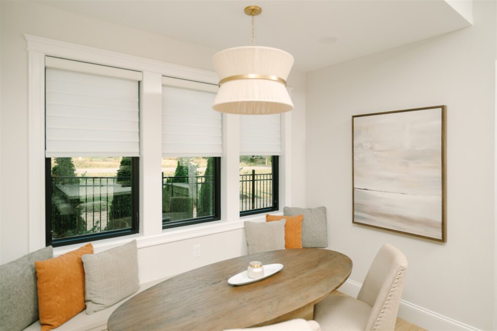 White Roman shades partly lowered to filter light in a dining nook.