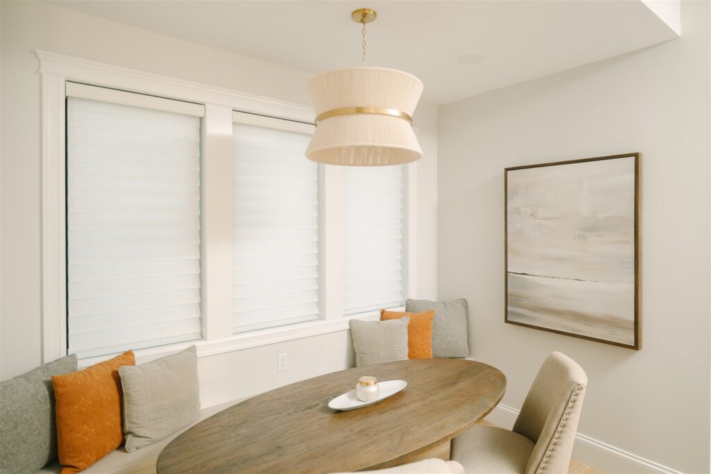 Dining nook with three white Roman shades lowered to matching heights.